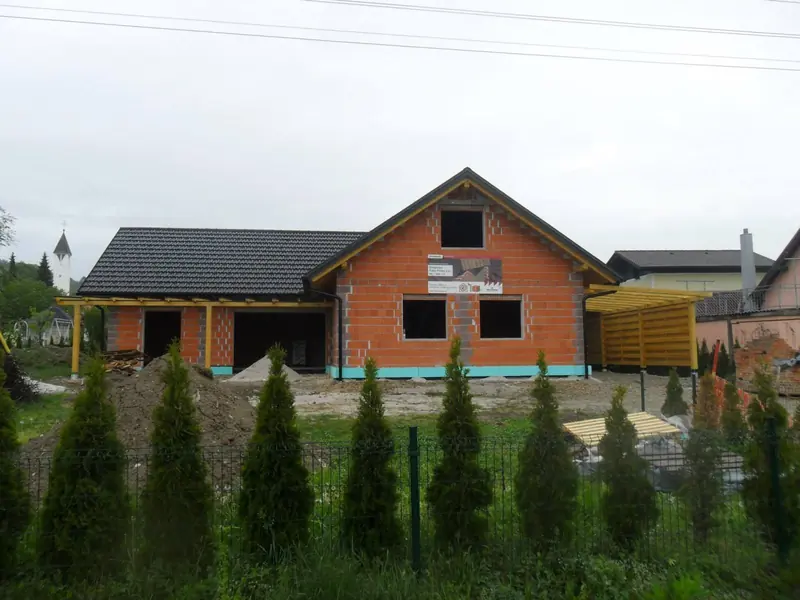 Opečna hiša s temno kritino in lesenim nadstreškom za avto