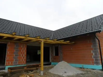 Hiša v obliki črke L s temno kritino in leseno pergolo