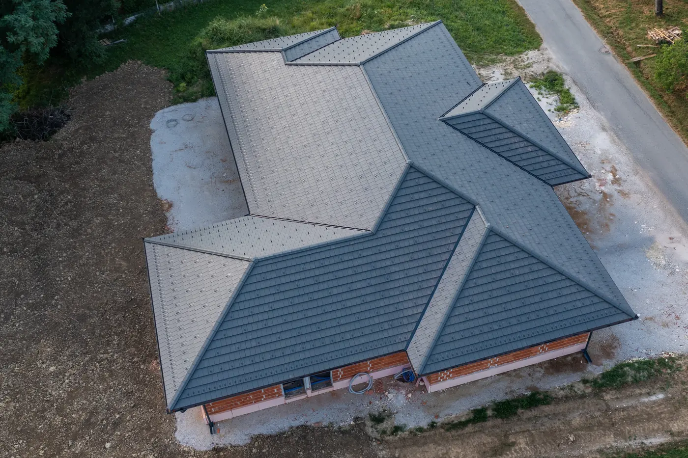 Nova večkapna streha s temno kritino in snegolovi na opečni hiši, posnetek od zgoraj